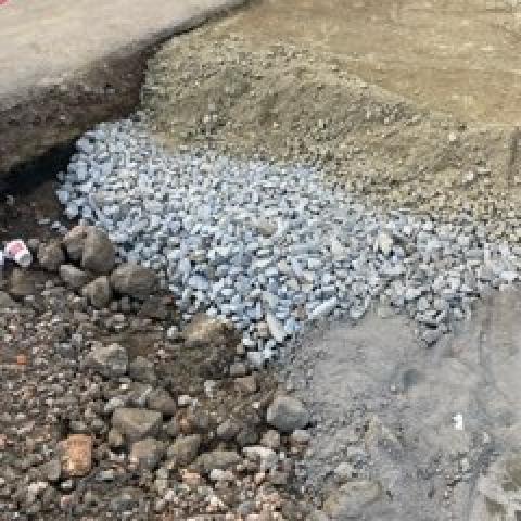 Chodnik przed tylnym wejściem do Centrum Sportu PP w trakcie przebudowy.  Na pierwszym planie widoczne warstwy nowej nawierzchni: istniejąca nawierzchnia, żwir, podsypka cementowo-piaskowa. 