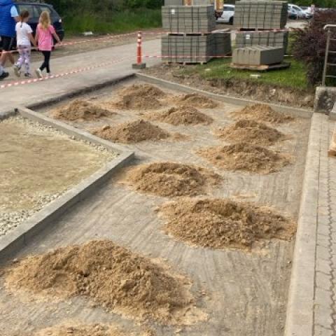 Chodnik przed tylnym wejściem do Centrum Sportu PP w trakcie przebudowy. Na pierwszym planie widać podłoże przygotowane do położenia kostki brukowej. Na wyrównaniej podsypce widać kopczyki piasku.