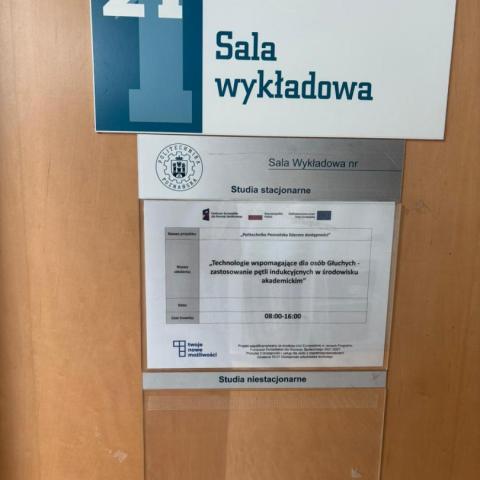 Zdjęcie. Etykieta drzwi z numerem sali wykładowej: 21. Przywieszka z tytułem szkolenia: "Technologie wspomagające dla osób Głuchych - zastosowanie pętli indukcyjnych w środowisku akademickim"
