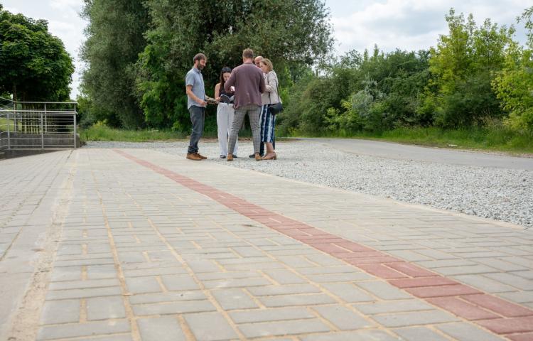 Grupka ludzi stoi na nowo wybudowanym chodniku