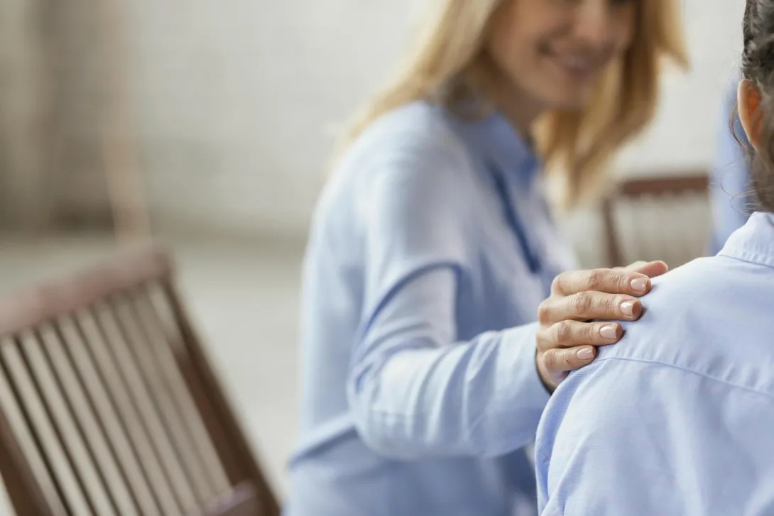 Kobieta trzyma ręke na ramieniu drugiej osoby.